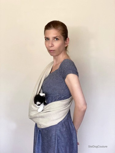 Kot siedzi w naturalnym lnianym nosidle na ramię